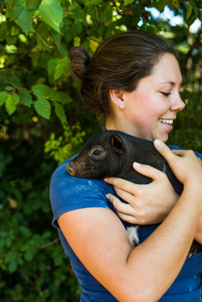 Intern holding a baby pig on her shoulder