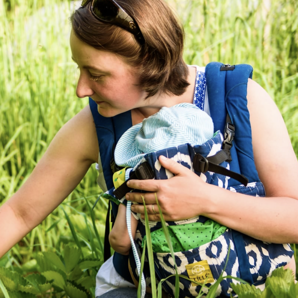 Photo of Allyson Angelini with a baby in a carrier, in a field