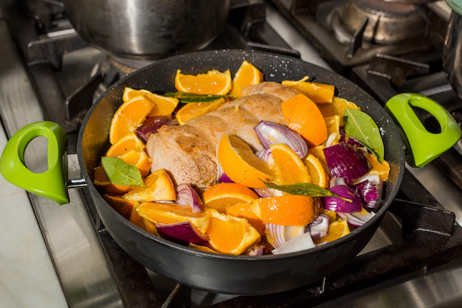 Pork loin, orange slices and red onions in a braising dish on the stove.