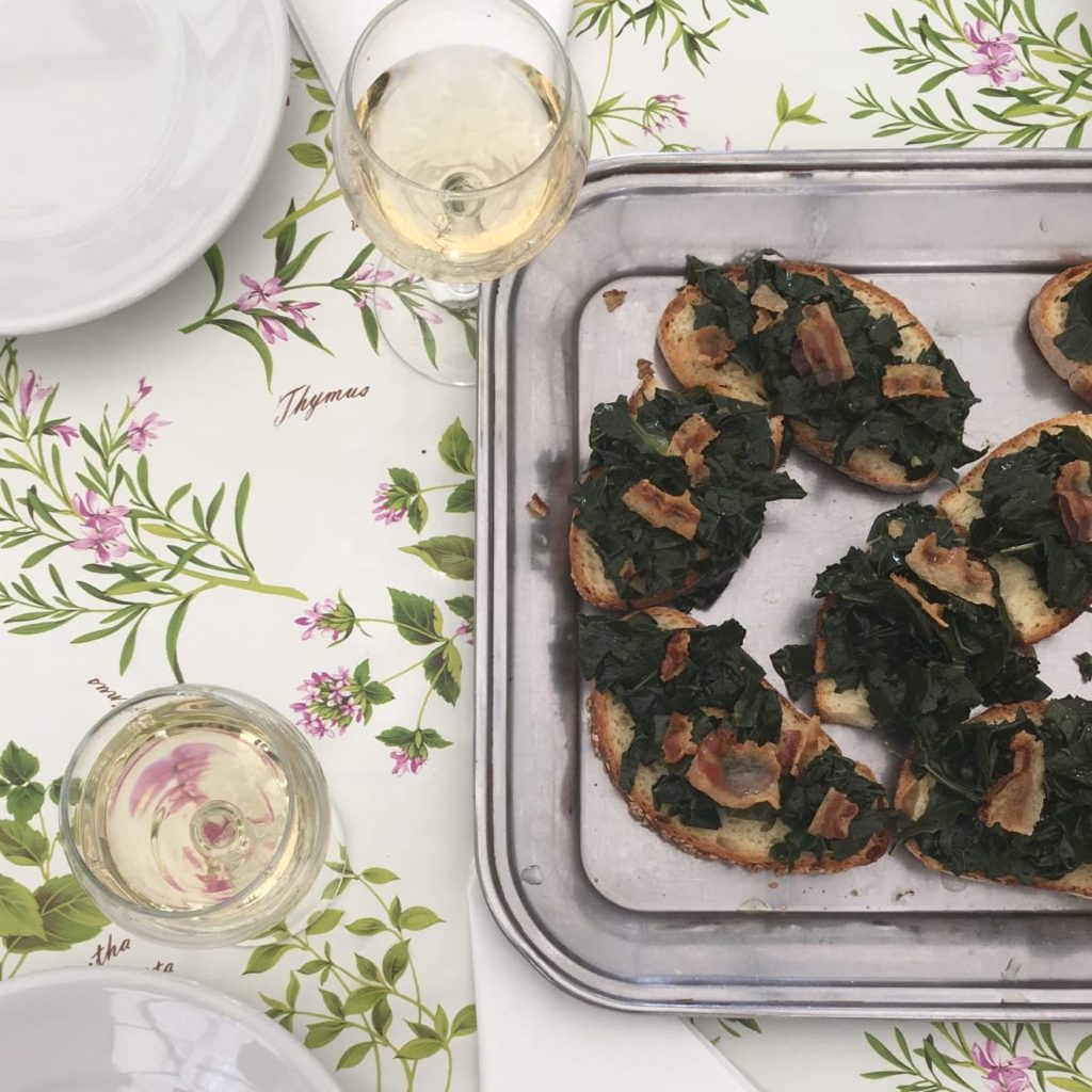 Table set with two glasses of white wine and a platter of cavolo nero crostone.