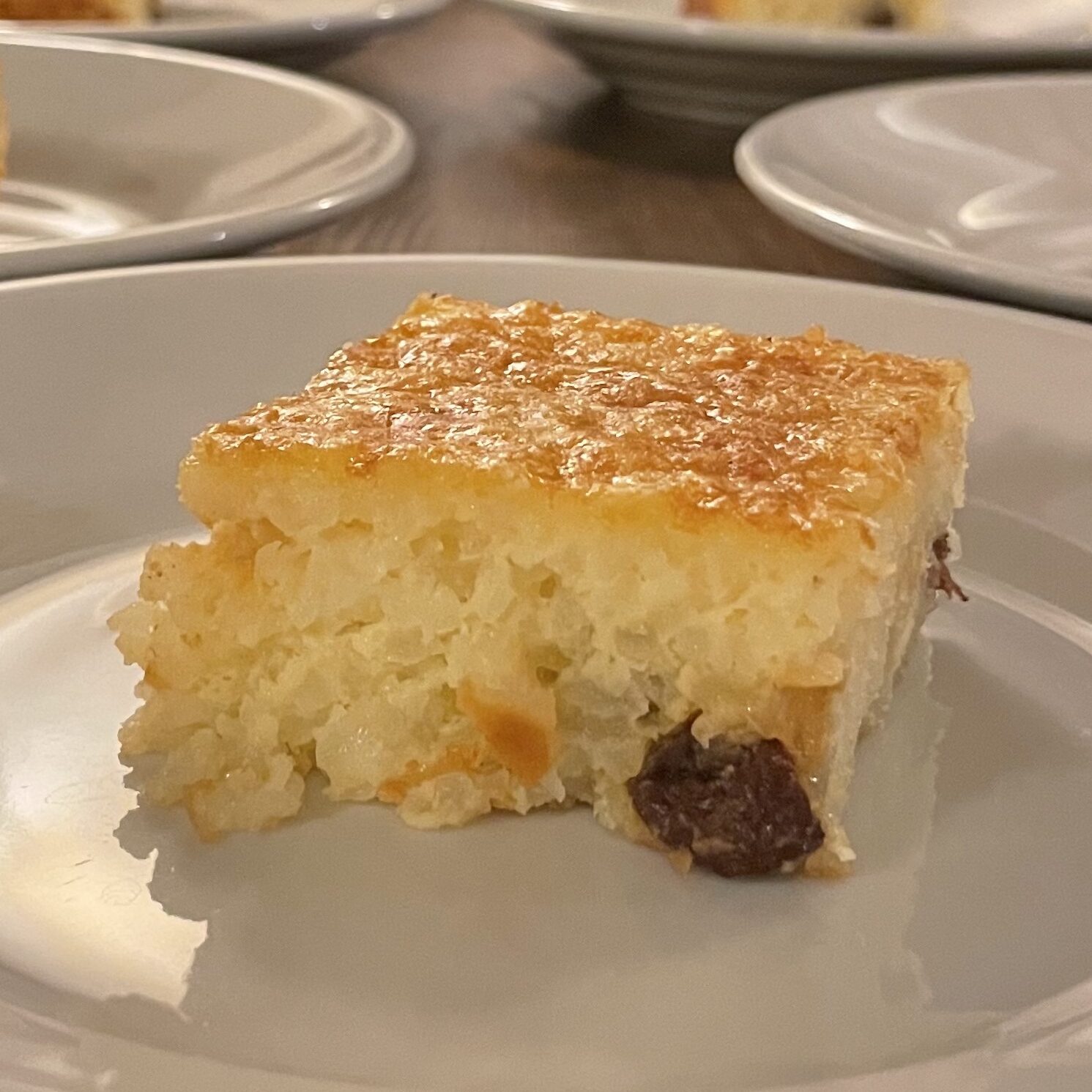 A square piece of the Dolce di Riso cake, with a gently browned top, grains of rice and speckled with raisins.