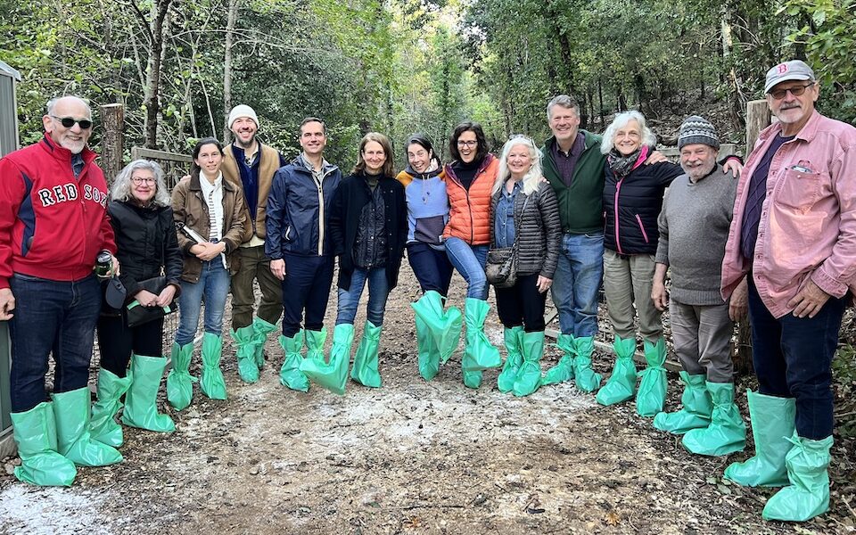 A photo of 13 people on a trail in the woods, all wearing green plastic booties.