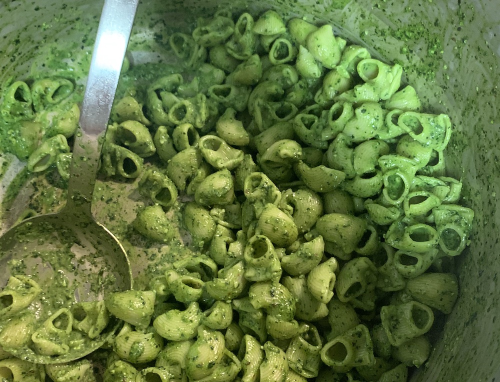 Chiocciole (snail) shaped pasta in a big pot, coated in bright green pesto, with a big metal serving spoon.