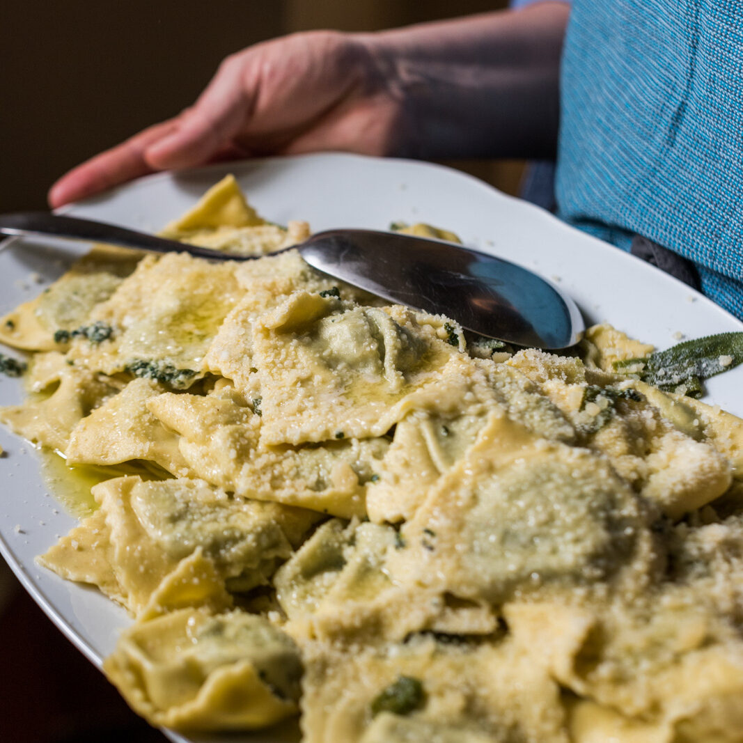 A close-up photo of someone holding a platter of ravioli sprinkled with cheese.