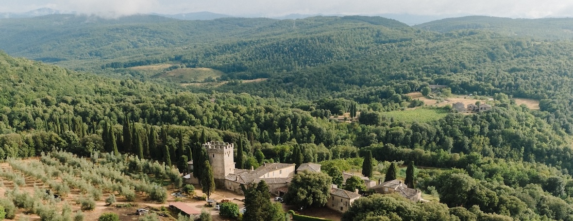 An aerial photograph of the Spannocchia castle with the expansive grounds surrounding it. The forested hills stretch out as far as can be seen.